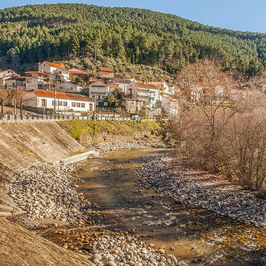 Paisaje rural idílico en la Serra da Estrela: río, casas tradicionales y naturaleza exuberante.