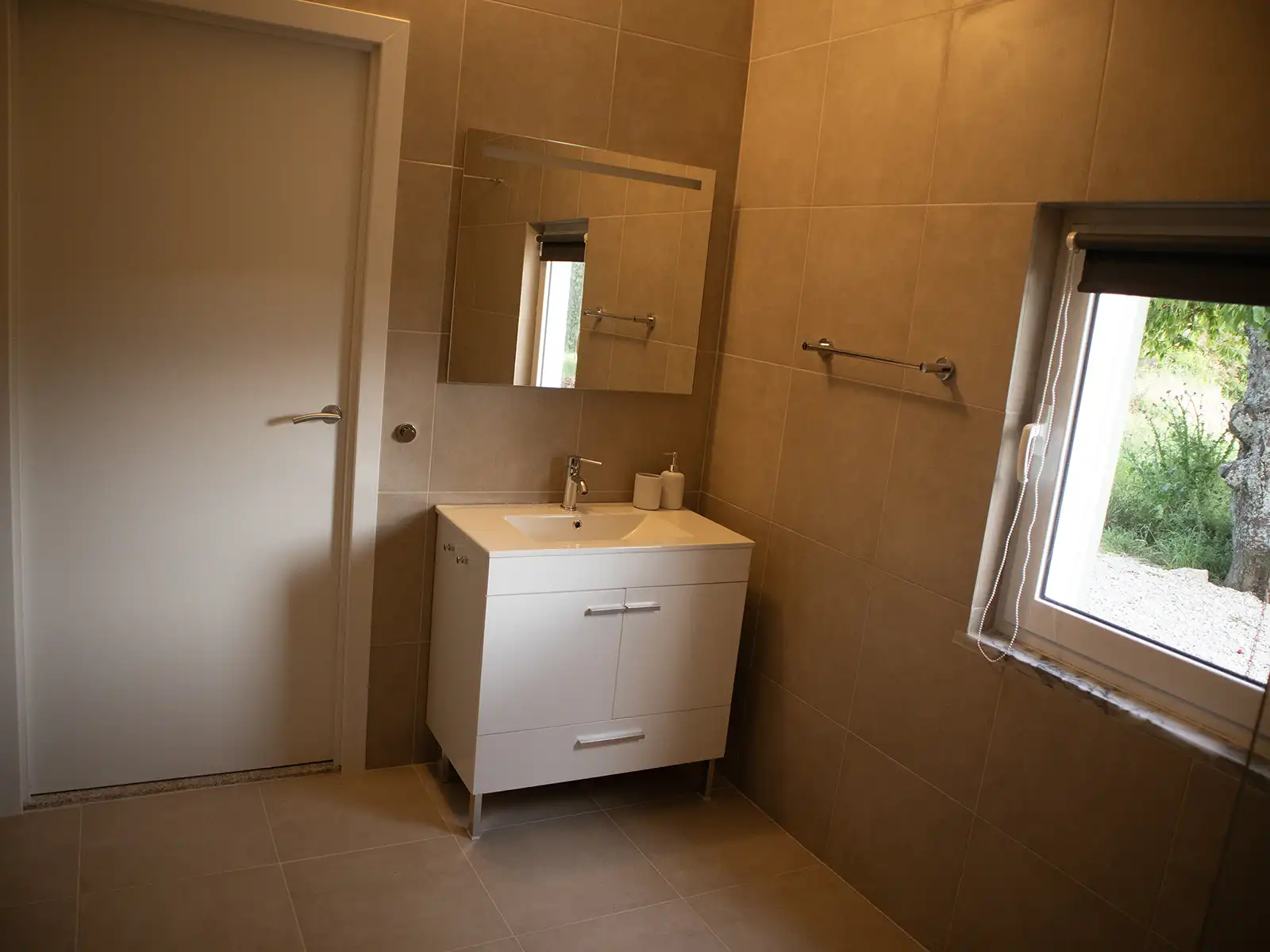 Licht en ruim: een rustgevende badkamer in de Serra da Estrela. Stijlvolle badkamer met veel licht, een spiegel en uitzicht op groene natuur.