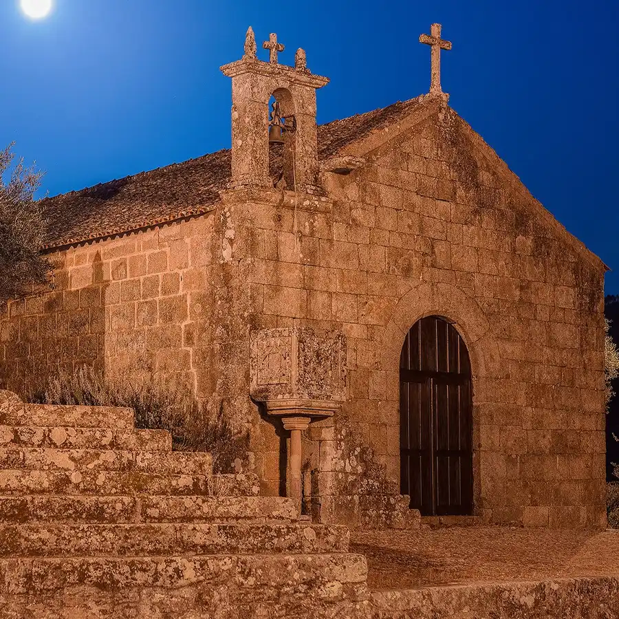 Igreja antiga iluminada sob um céu estrelado, refúgio de paz na Serra da Estrela.